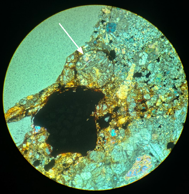 smaller chrondrule with many different shapes of light grey crystals with arrow indicating it